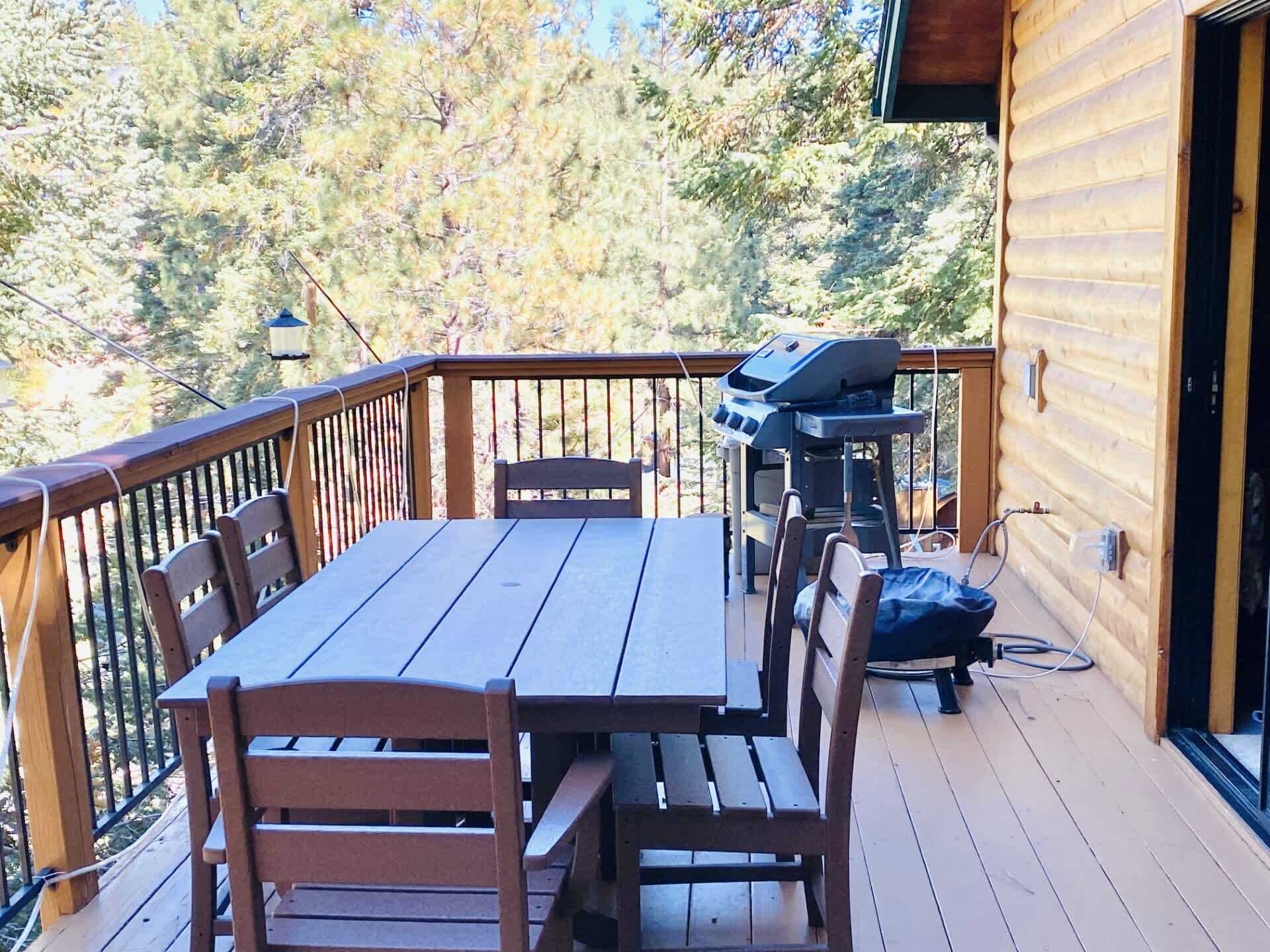 A wooden deck with a table and chairs, a grill, and a view of trees.