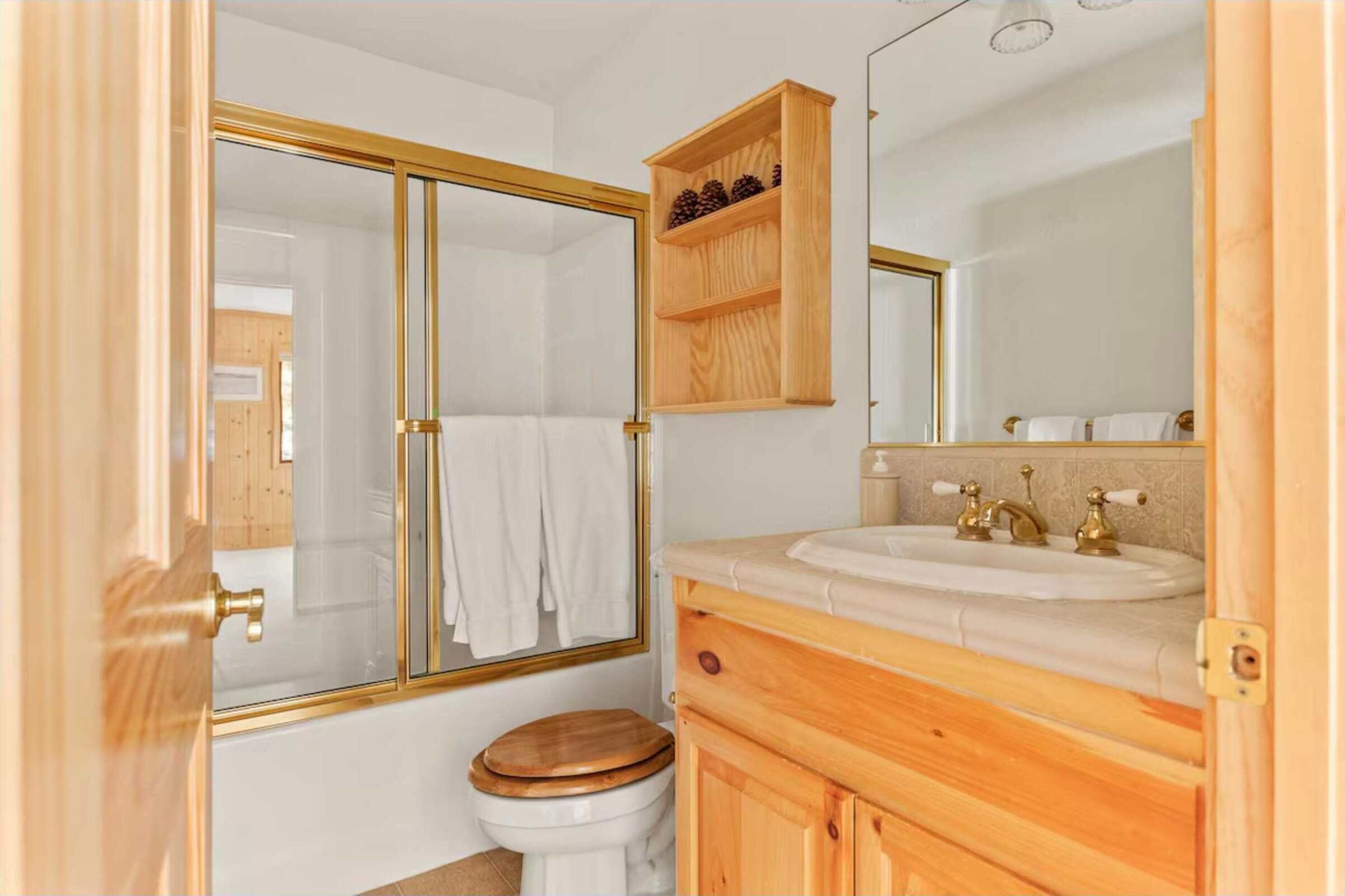 A bathroom with a wooden vanity, a white sink, a mirror, and a glass shower enclosure.