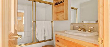 A bathroom with a wooden vanity, a white sink, a mirror, and a glass shower enclosure.