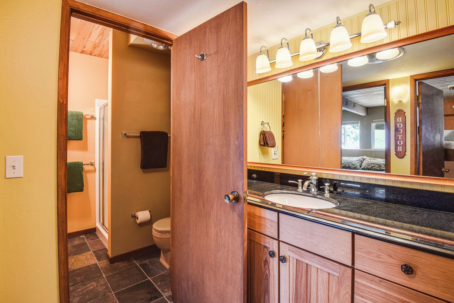 A bathroom with a wooden vanity, a sink, a toilet, and a mirror with lights.