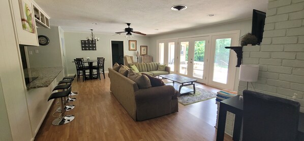 A spacious living room with a large sofa, a dining table, and a kitchen area. - Bamboo Terrace: Swimming Pool, Billiards, Darts (Bedford)