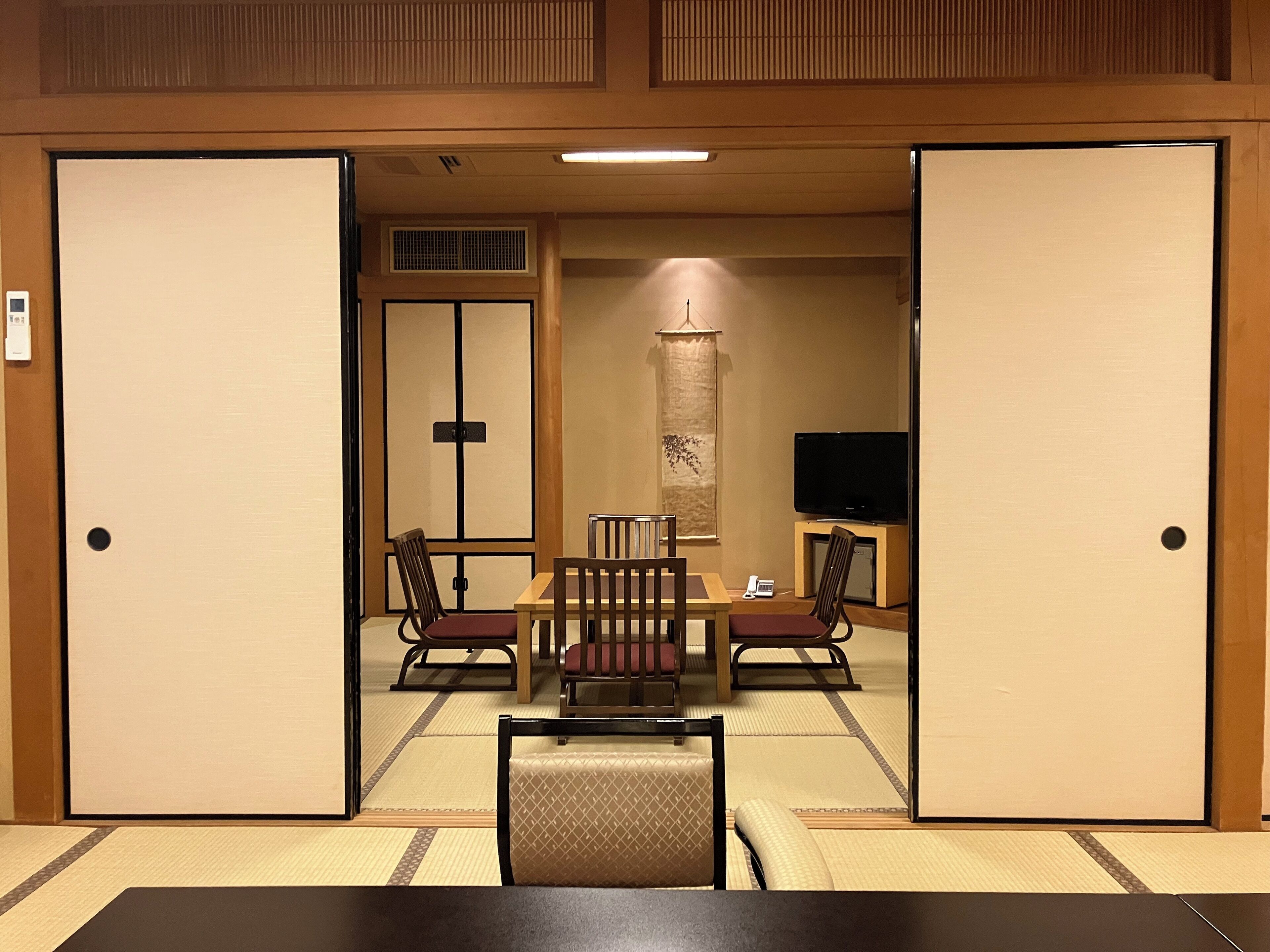 A traditional Japanese room with tatami flooring, a low table with chairs, a television, and sliding doors.