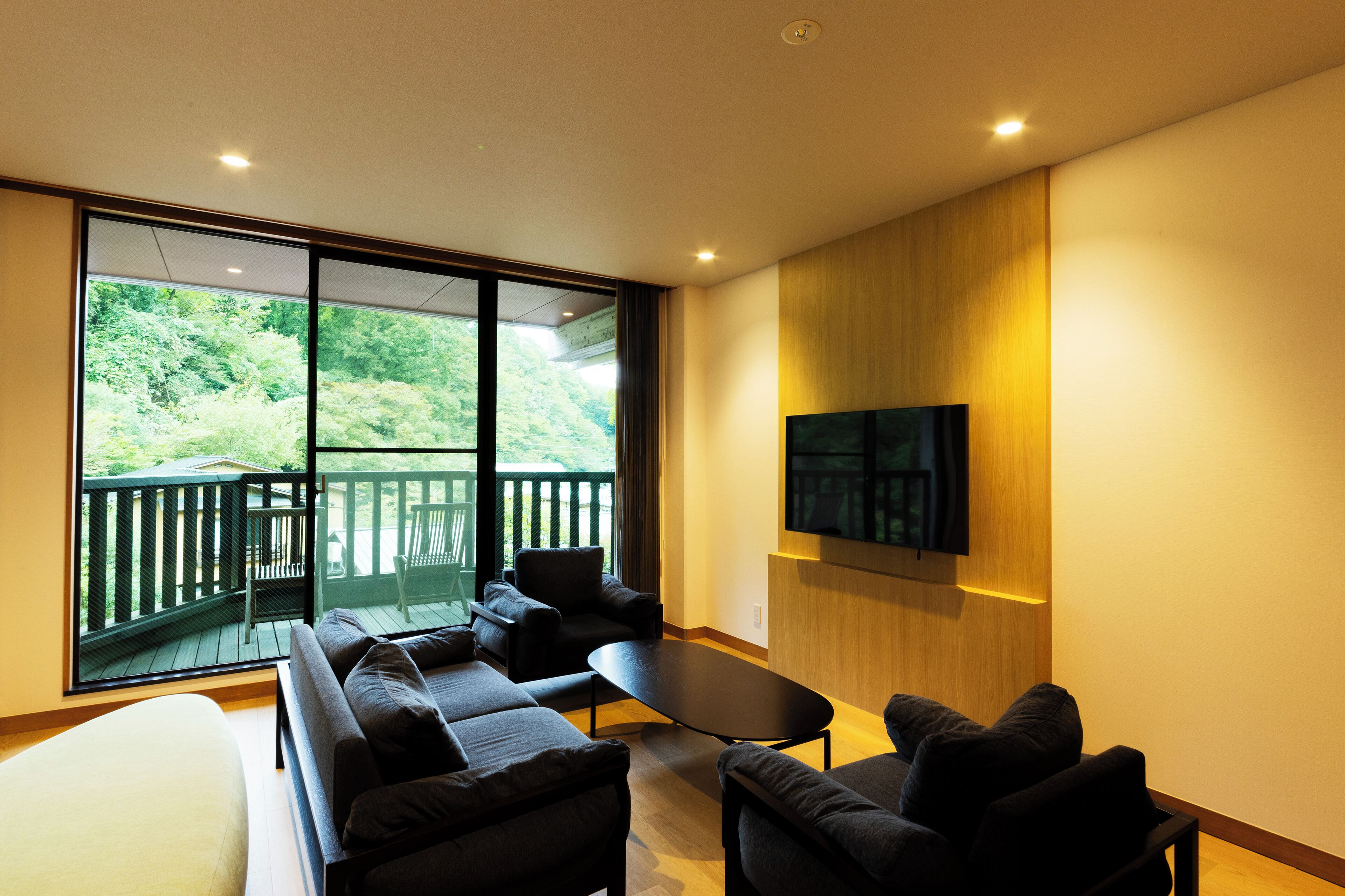 Una sala de estar moderna con un amplio ventanal corredero que da a un balcón, un televisor de pantalla plana montado en la pared y un conjunto de sofás.