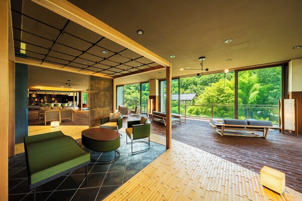 A spacious indoor area with a large window offering a view of greenery outside. There are seating areas with cushions and a dining table.