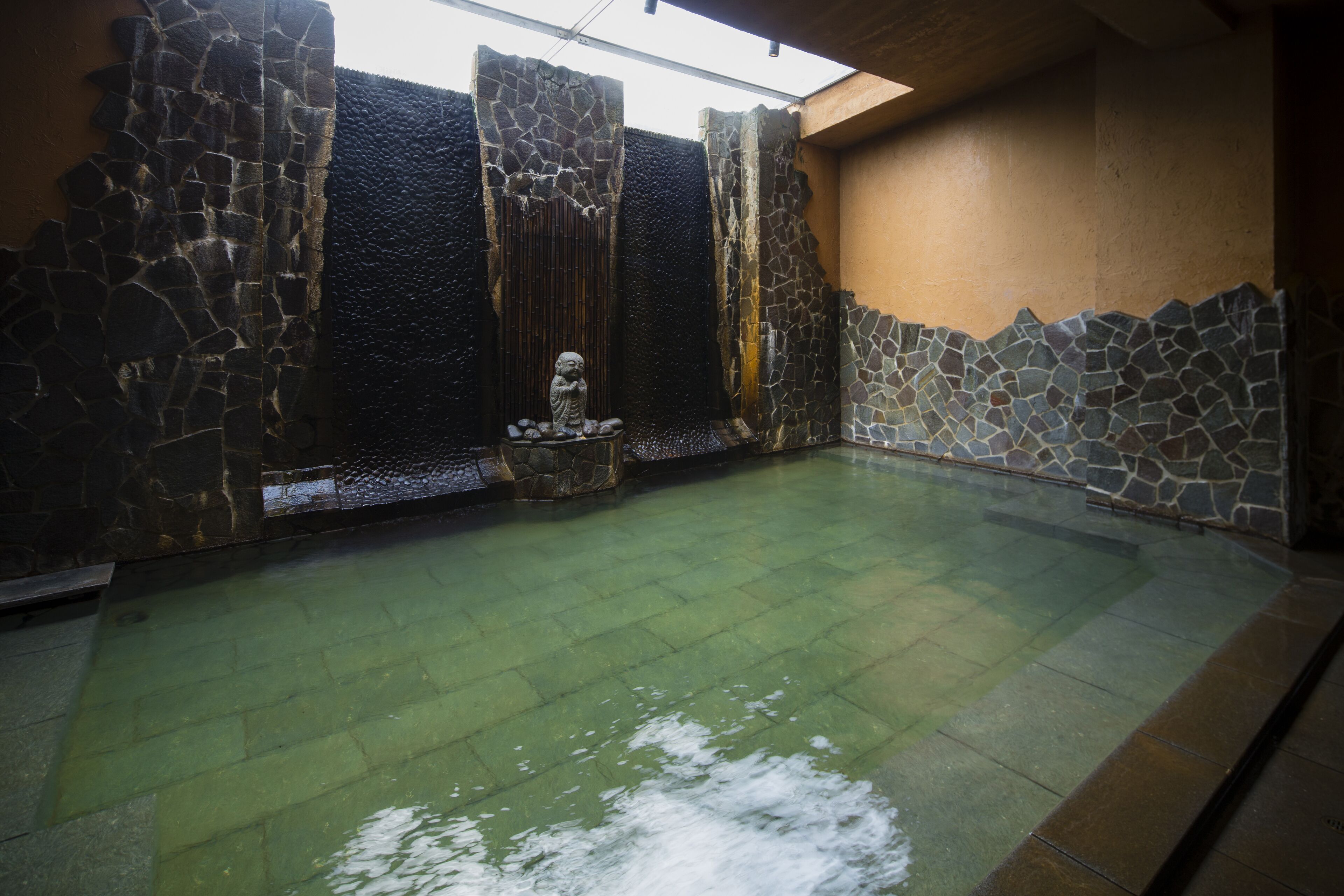 Una piscina interior con paredes de piedra, superficie de agua cristalina y una estatua en el centro.