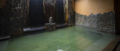 Una piscina interior con paredes de piedra, superficie de agua cristalina y una estatua en el centro.