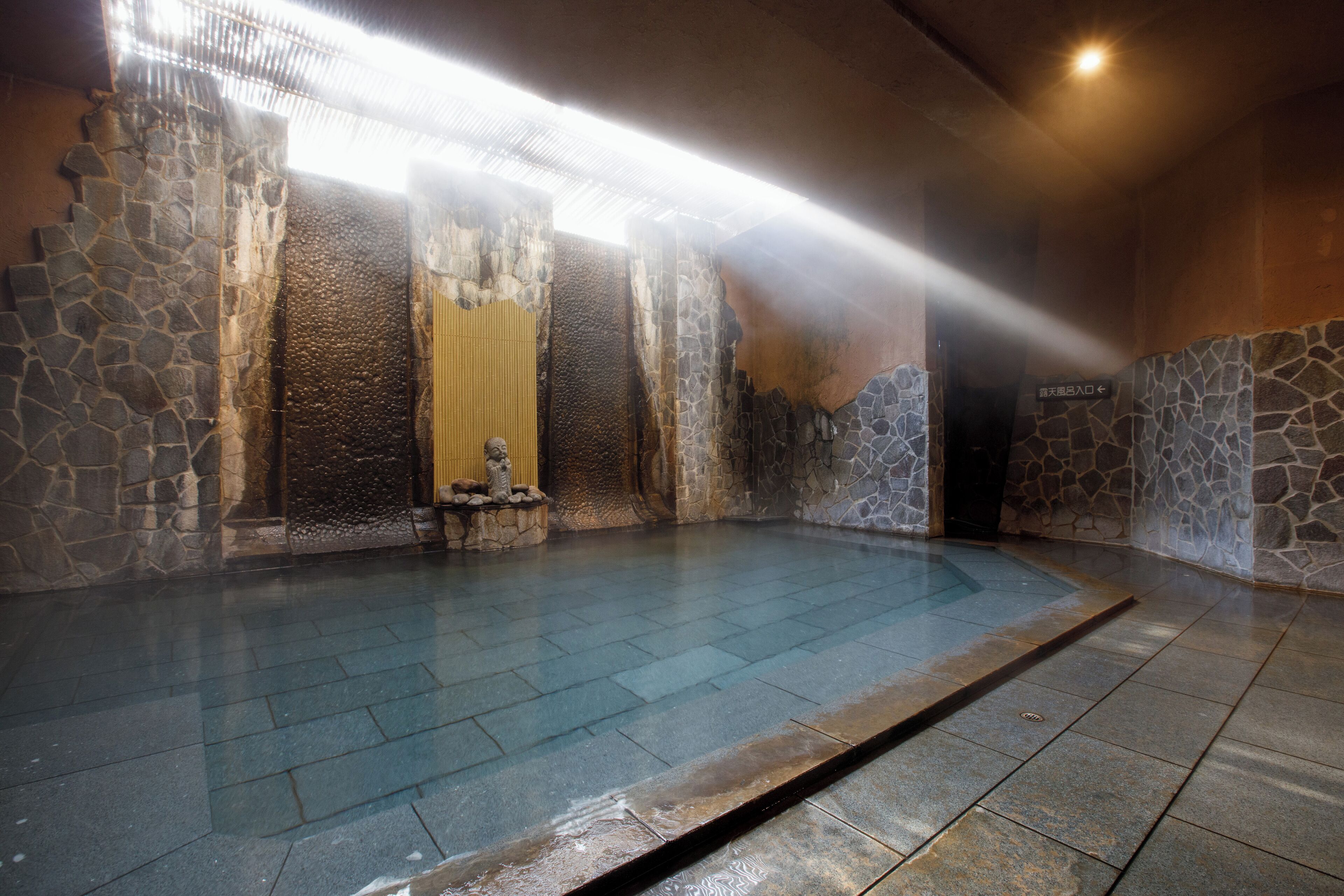 A stone-walled indoor pool with a clear blue floor, a stone bench, and a yellow curtain.