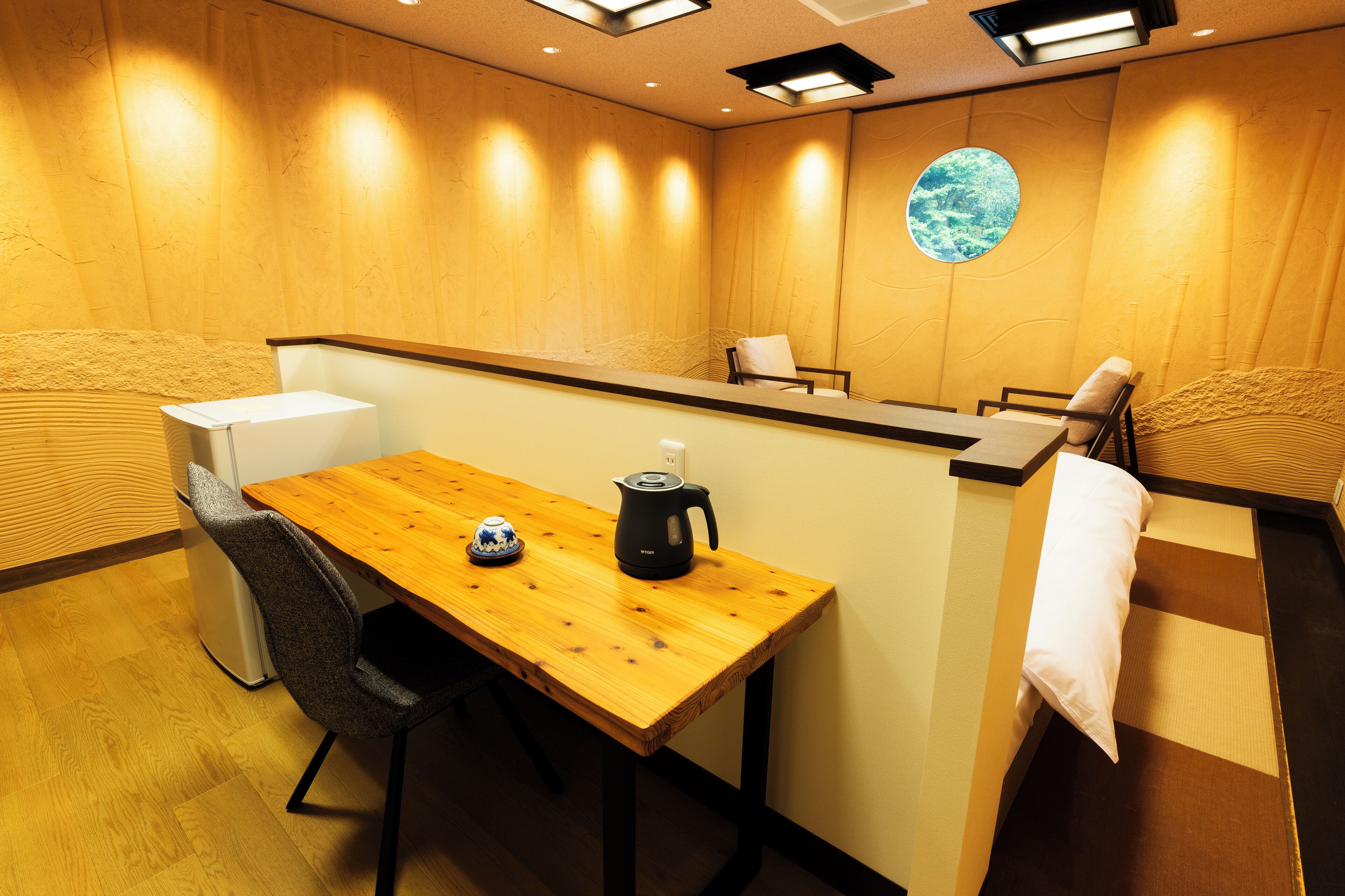 A wooden reception desk with a kettle and teapot, a small refrigerator, and a chair.