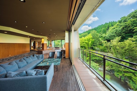 A modern hotel lobby with a long blue sofa, a small table, and a view of a forested area through large windows.