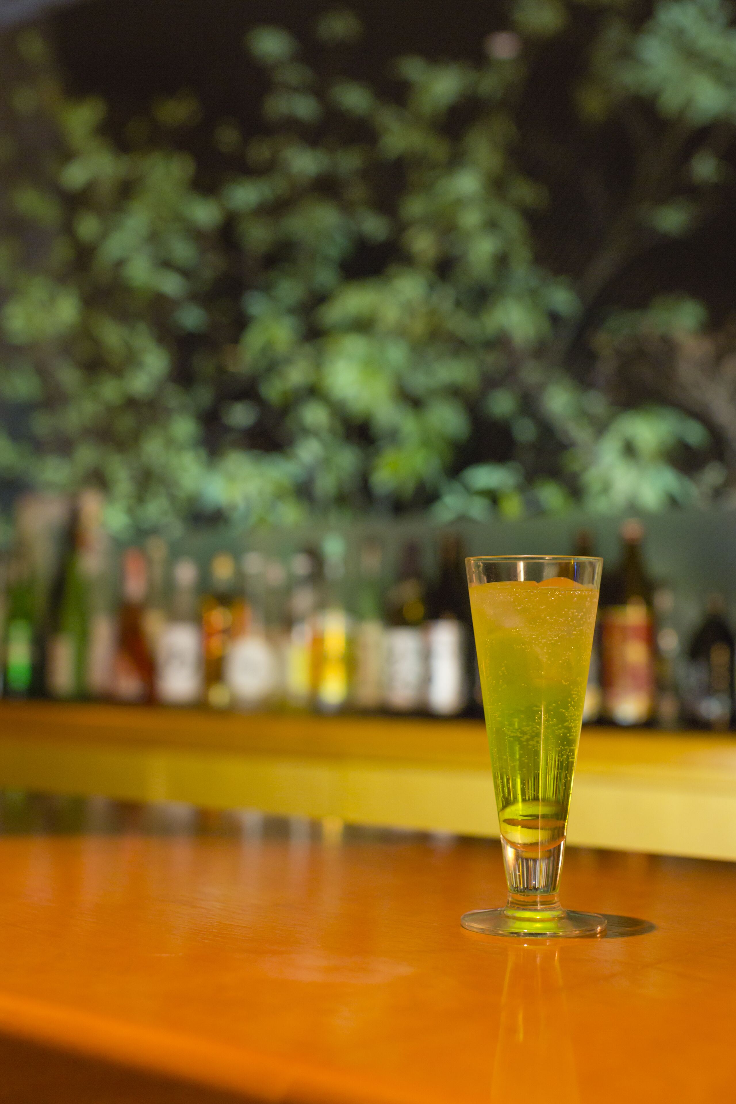 A bar setting with a glass of green beverage on a wooden surface.