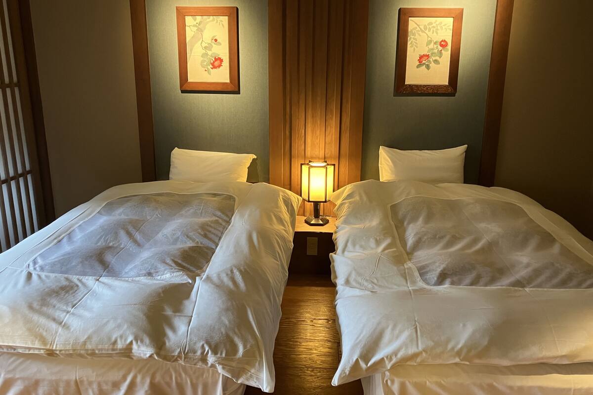 Een hotelkamer met twee bedden, een nachtkastje met een lamp, en twee florale afbeeldingen in lijsten aan de muren.