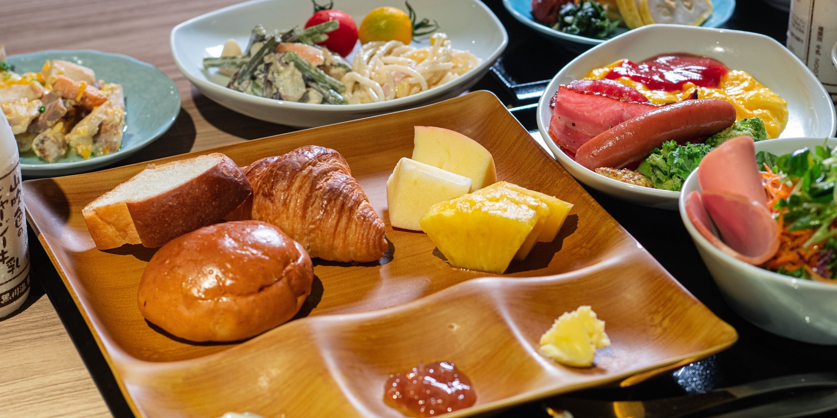Uma refeição com pão, croissants, queijo e fiambre numa bandeja de madeira.