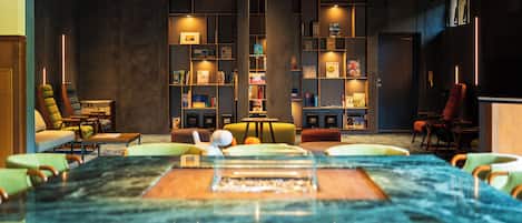 A modern interior with a large marble table, multiple seating areas, and a bookshelf filled with books.