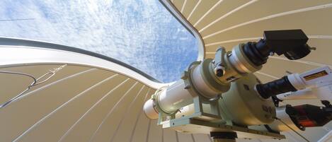 Un télescope installé sous un plafond incurvé, permettant d’observer le ciel par une fenêtre.