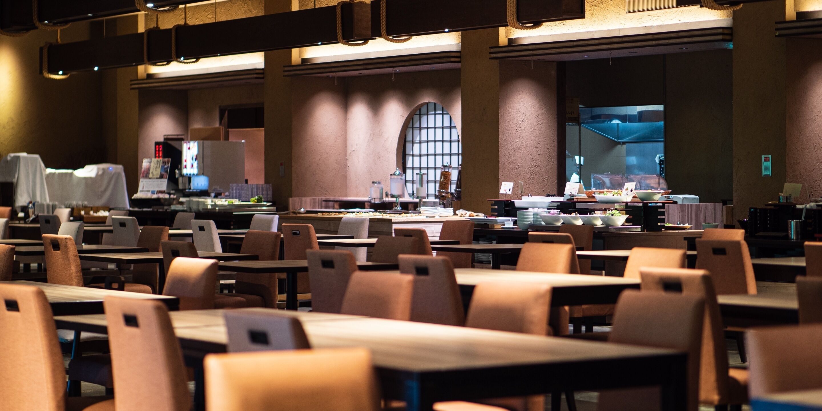 A spacious dining area with multiple tables and chairs, a large window with arched design, and a counter with food displays.
