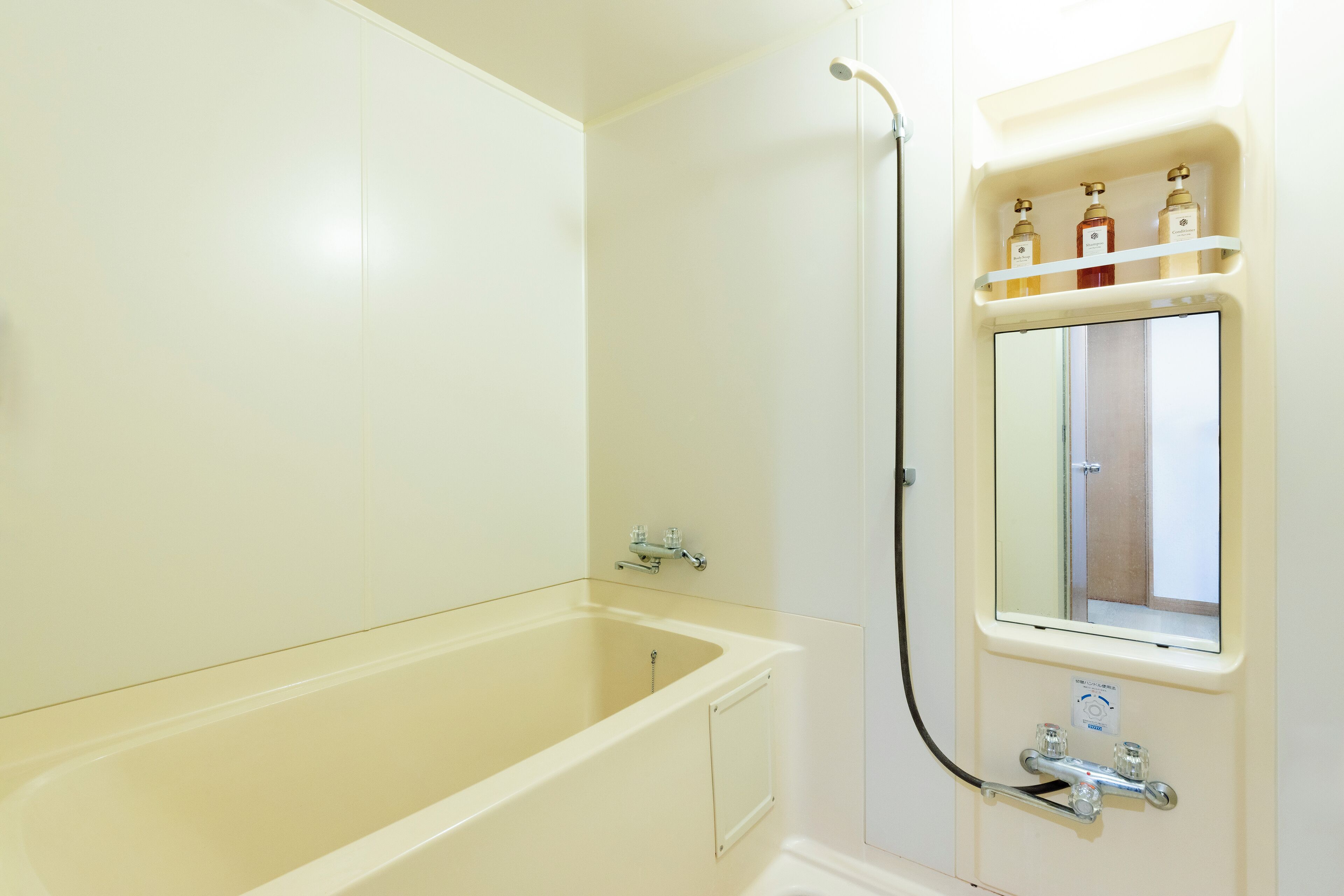 A bathroom with a bathtub, a shower, and a mirror with a shelf above it.