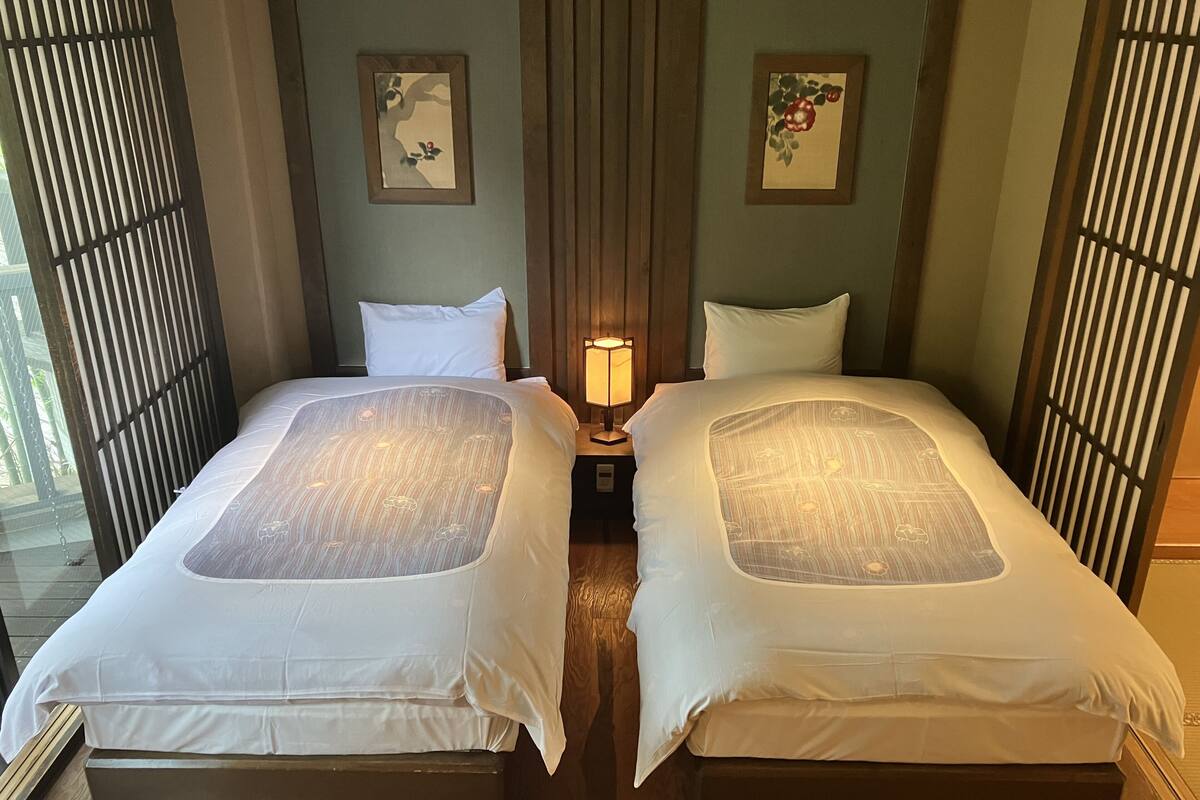 Een hotelkamer met twee bedden, een nachtkastje met een lamp en twee aan de muur hangende schilderijen.