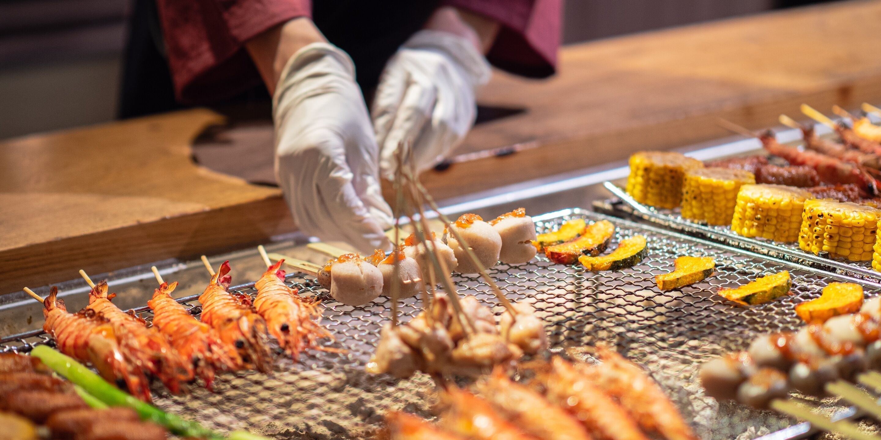 A person grilling various seafood items including shrimp and corn on a grill.