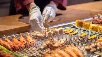 A person grilling various seafood items including shrimp and corn on a grill.
