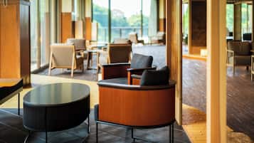 Un vestíbulo de hotel moderno con una mesa redonda, asientos cómodos y grandes ventanales con vistas al exterior.