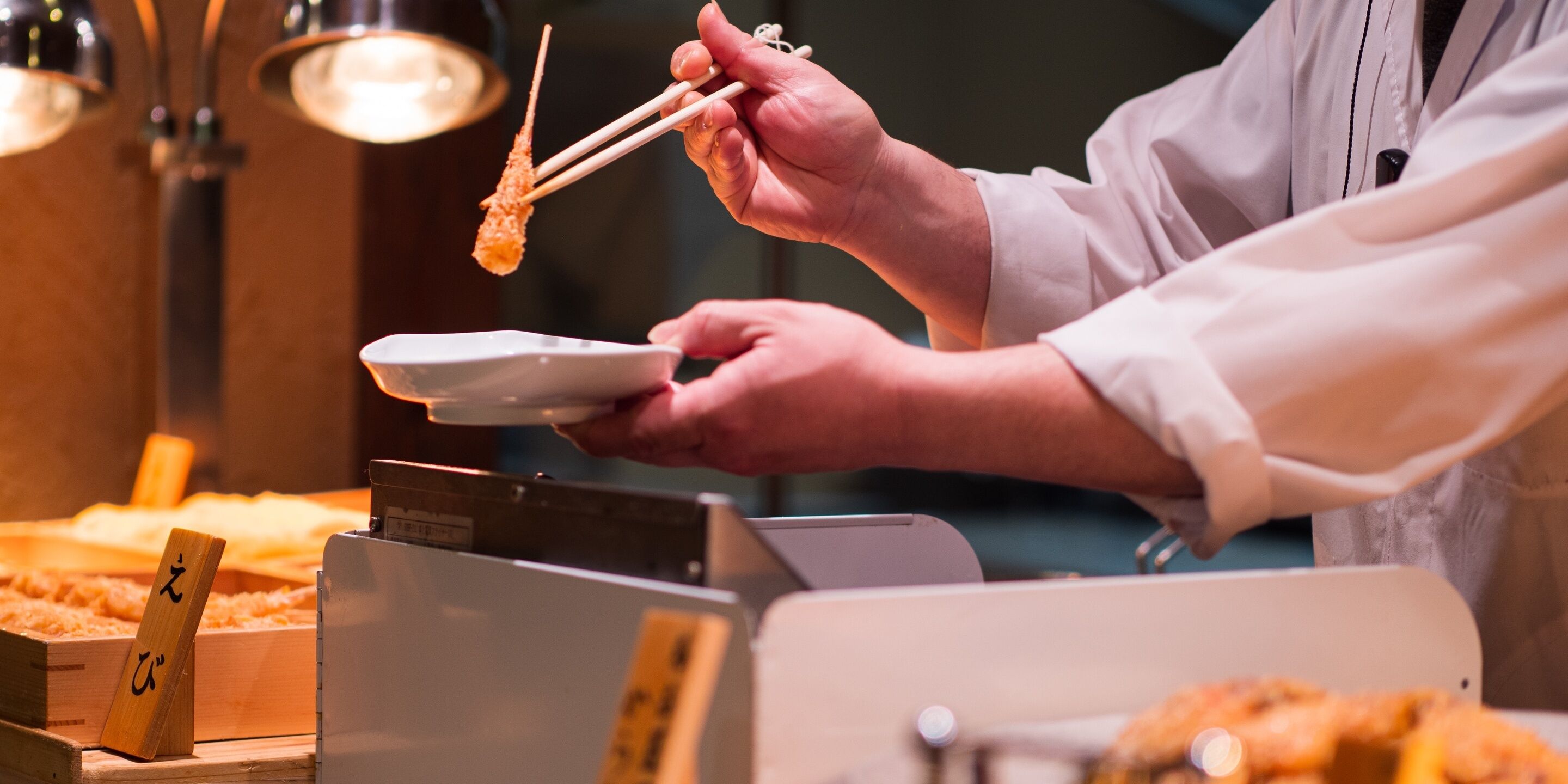 Iemand serveert eten met stokjes, een bord en een doos met etenswaren.
