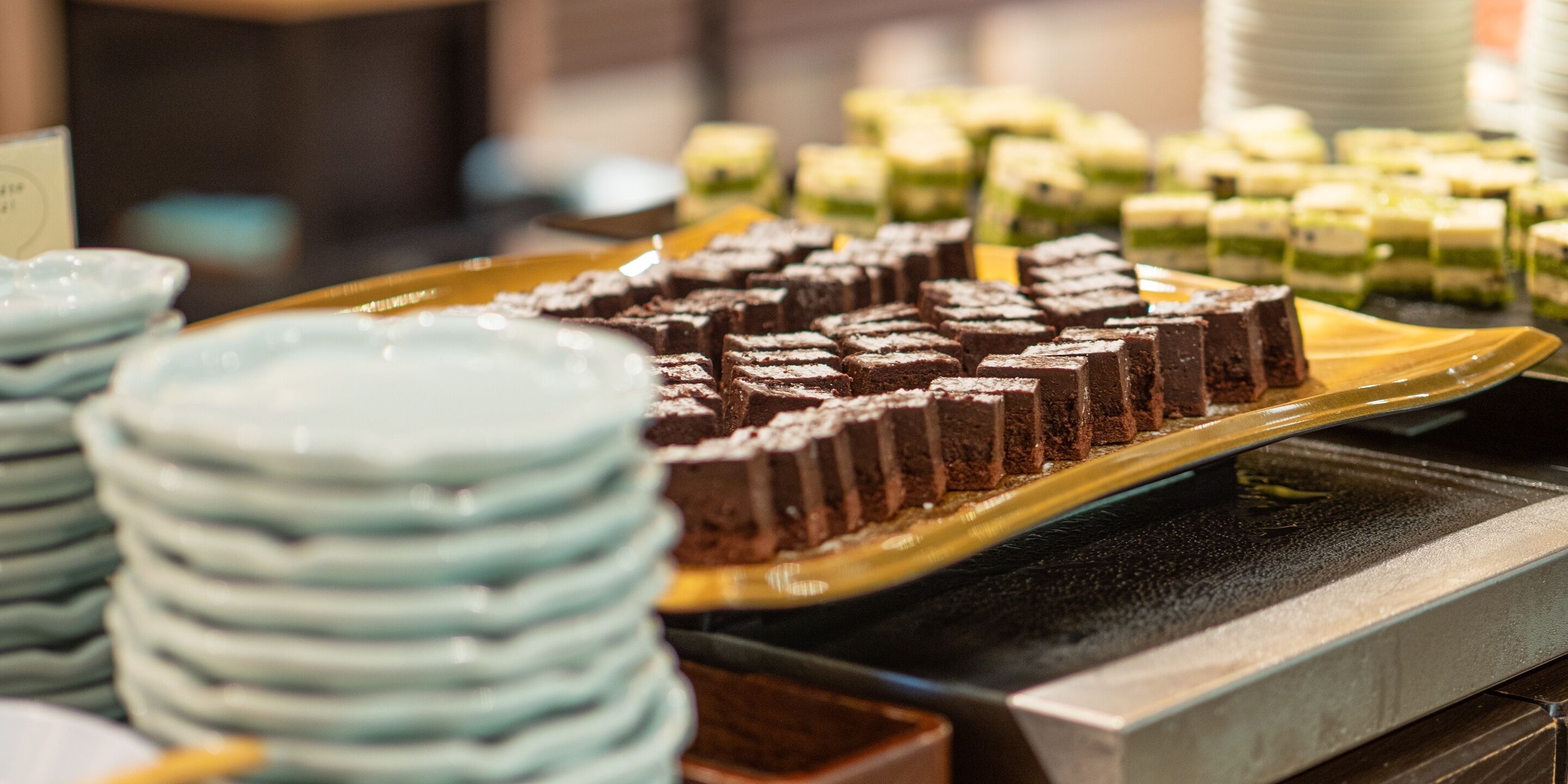 En buffet med forskellige desserter, herunder chokoladebrownies og kager med grøn glasur, anrettet på tallerkener.