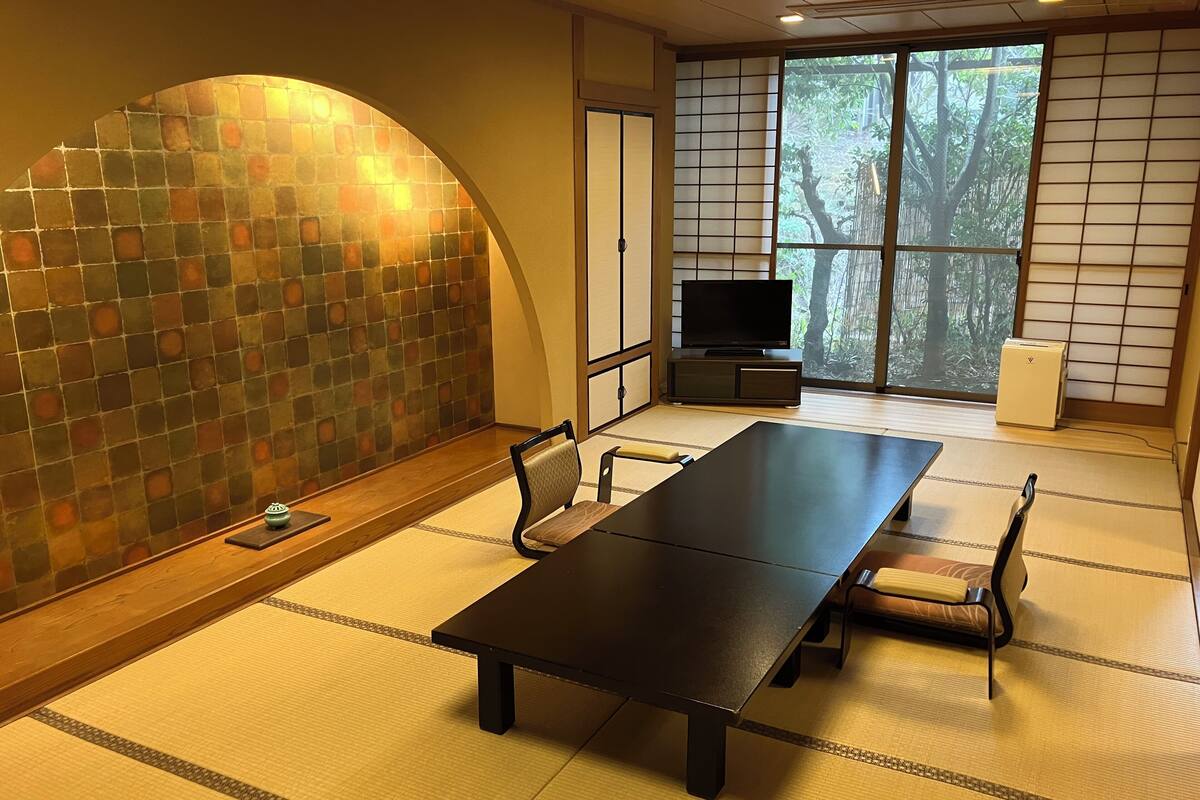 Een traditionele Japanse kamer met tatami vloerbedekking, een lage tafel en een televisie op een standaard.