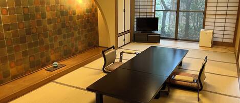 A traditional Japanese-style room with tatami flooring, a low table, and a television on a stand.
