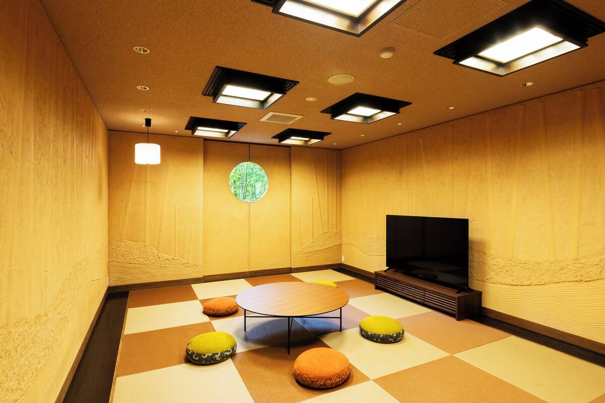 Een kamer met een ronde tafel, vier ottmanen, een flatscreen televisie en een ronde decoratie aan de muur.