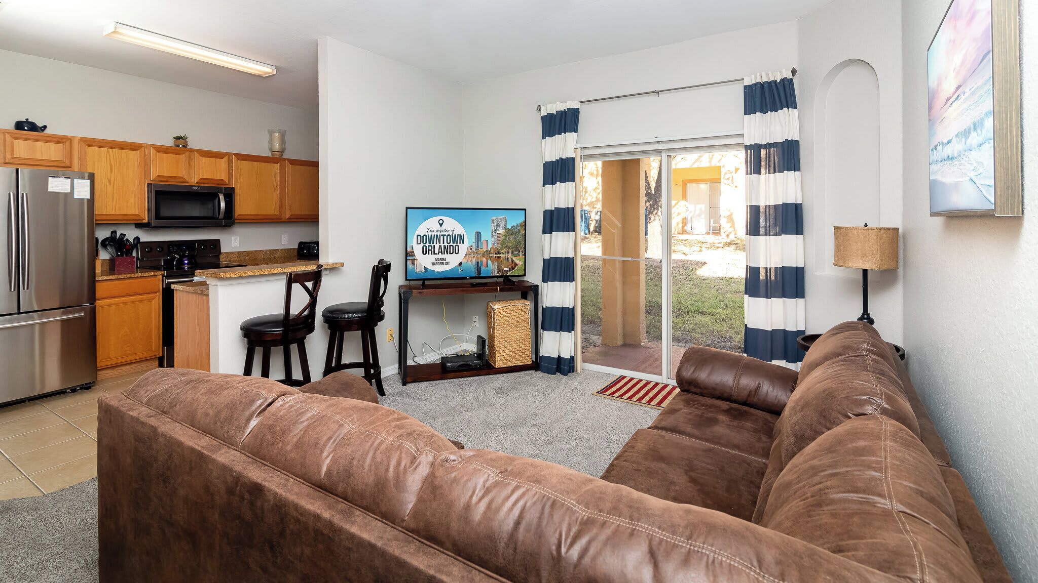 Ein gemütlicher Wohnraum mit Küchenzeile, einem braunen Ledersofa, einem Fernseher und Blick ins Freie.