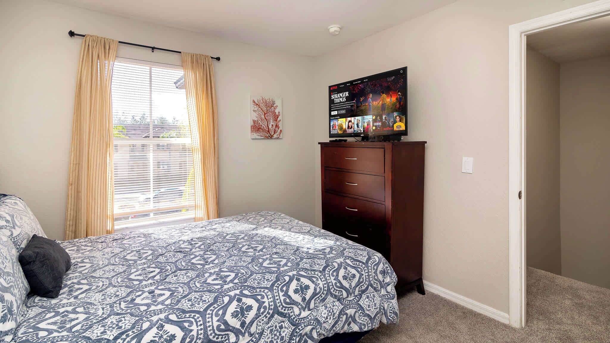 A bedroom with a bed, a dresser, a TV on the dresser, and a window with curtains.