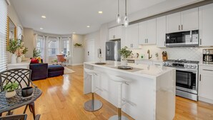A modern kitchen with white cabinets, stainless steel appliances, and a central island with bar stools. - Palmer Square 1BR w/ Private Patio (Princeton)