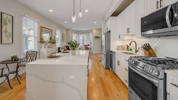A modern kitchen with white cabinets, a large island, stainless steel appliances, and wooden flooring. - Palmer Square 1BR w/ Private Patio (Princeton)