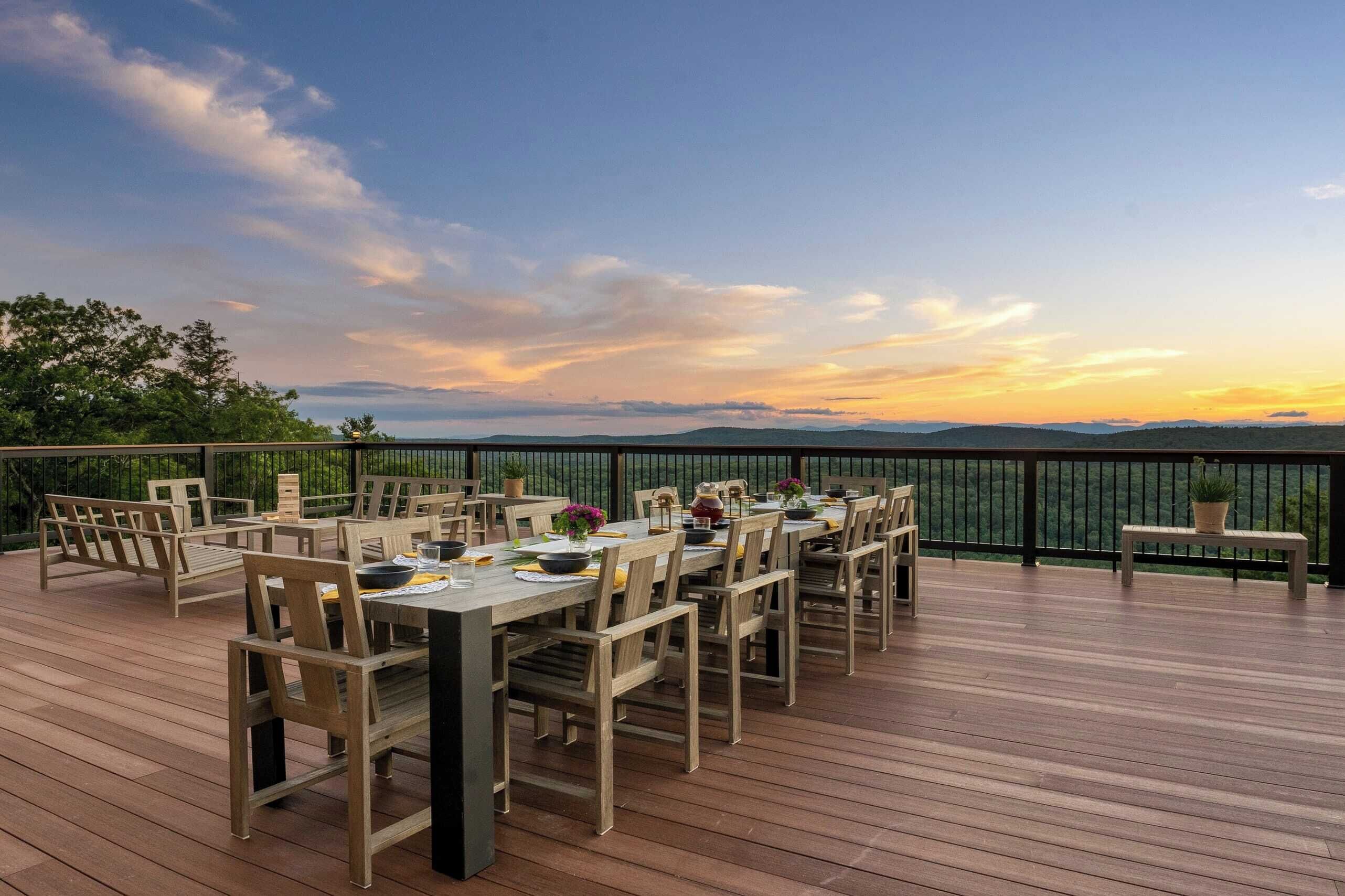 An outdoor dining area with wooden tables and chairs, a view of the mountains, and a railing.