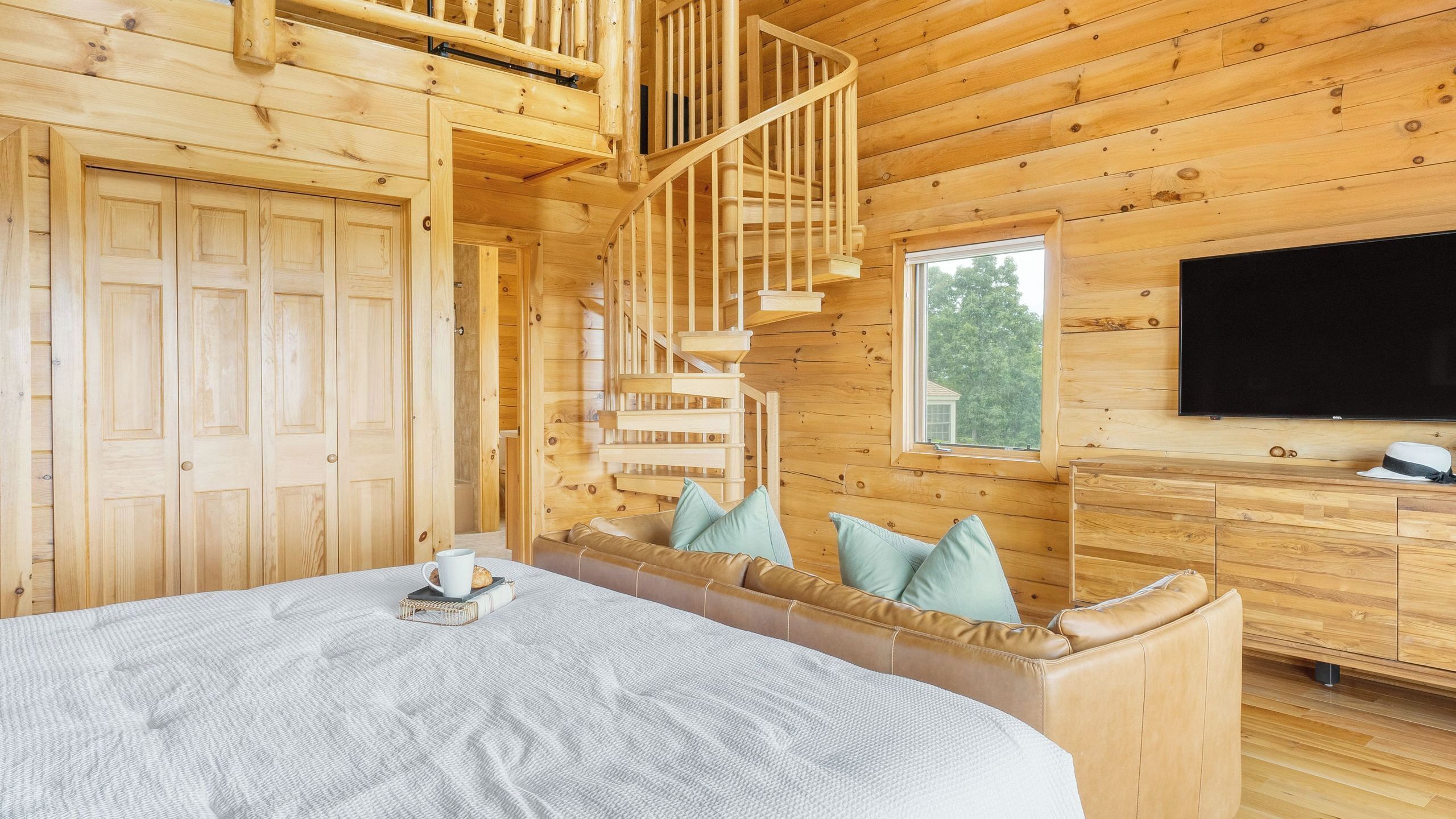 Een houten blokhut met een bed, een ingebouwde bank, een trap en een televisie.