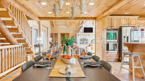 A wooden interior with a dining table set for six, a fireplace, and a kitchen area.