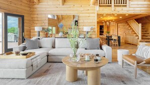 A log cabin interior with a living area featuring a sectional sofa, a round coffee table, and a dining area with a table and chairs.