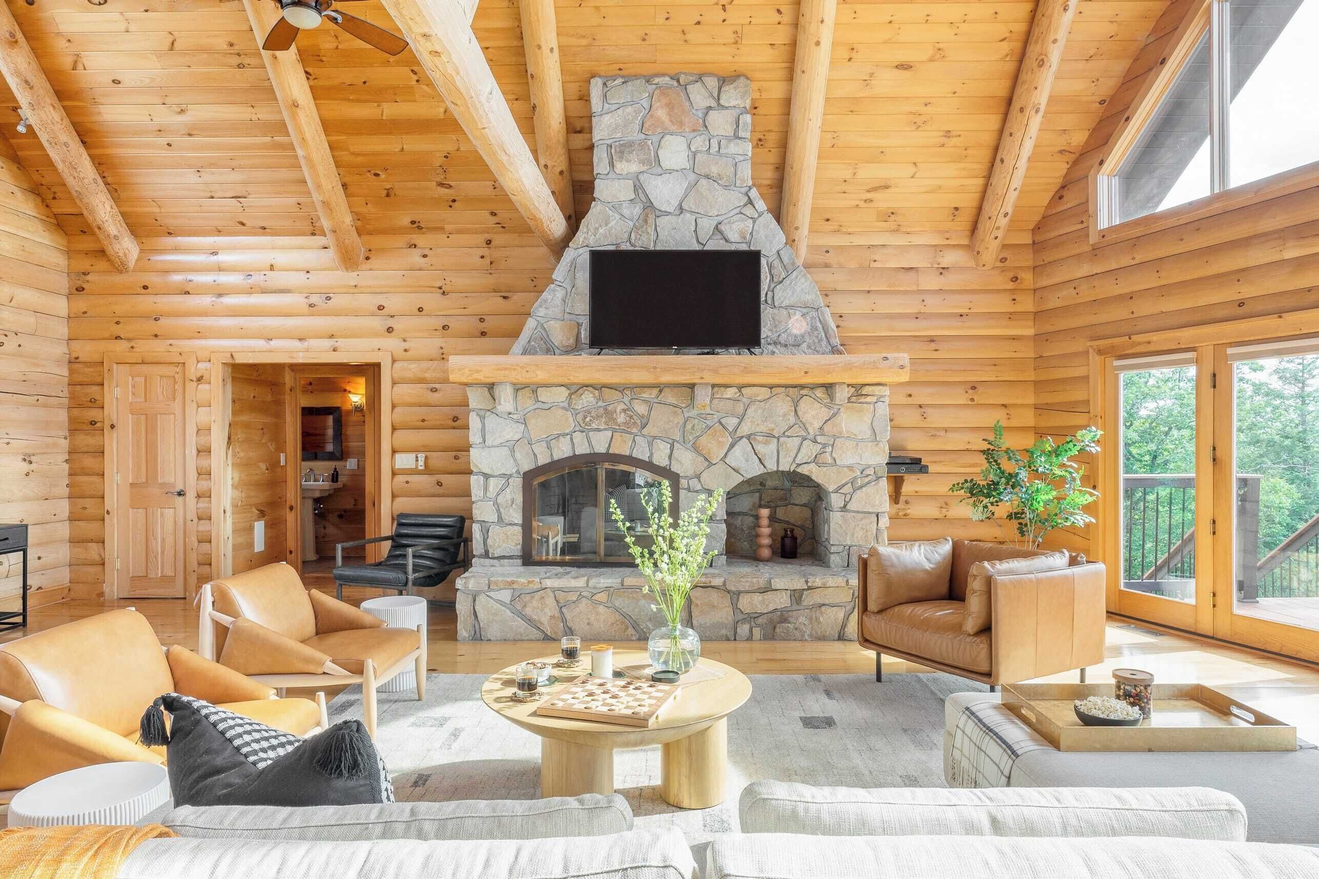L’intérieur d’une cabane en rondins, avec une cheminée en pierre, des meubles en cuir et un téléviseur fixé au-dessus.