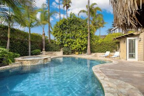 Una piscina de borde curvo, rodeada de palmeras y un jardín bien cuidado.