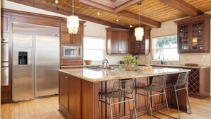 A spacious kitchen with a large island, wooden cabinets, stainless steel appliances, and a hanging light fixture. - Wavebreak by Avantstay Close to Beaches/surfing (Solana Beach)