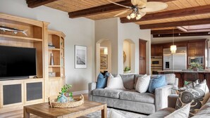 A living room with a grey sofa, wooden coffee table, and a TV on a wooden cabinet. There is a kitchen visible in the background with modern appliances. - Wavebreak by Avantstay Close to Beaches/surfing (Solana Beach)