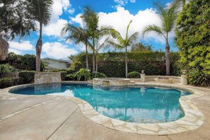 Piscina con borde de piedra, rodeada de palmeras y un muro de piedra.