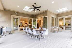 A spacious patio with a dining table, white chairs, and a ceiling fan. - Birdie by Avantstay Group Retreat at Hilton Head (Hilton Head Island)