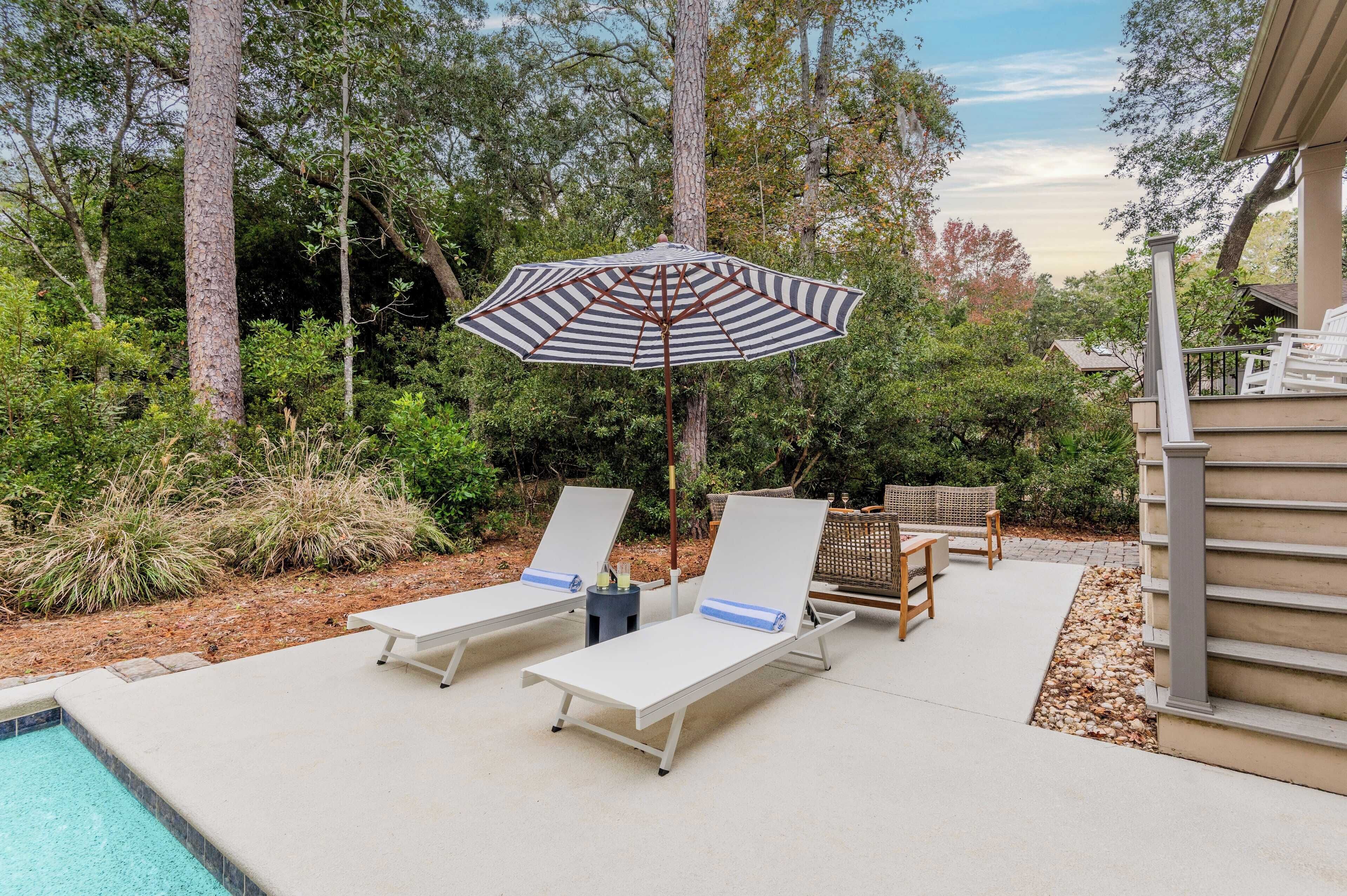 A poolside area with two sun loungers, a striped umbrella, and a small table with drinks.
