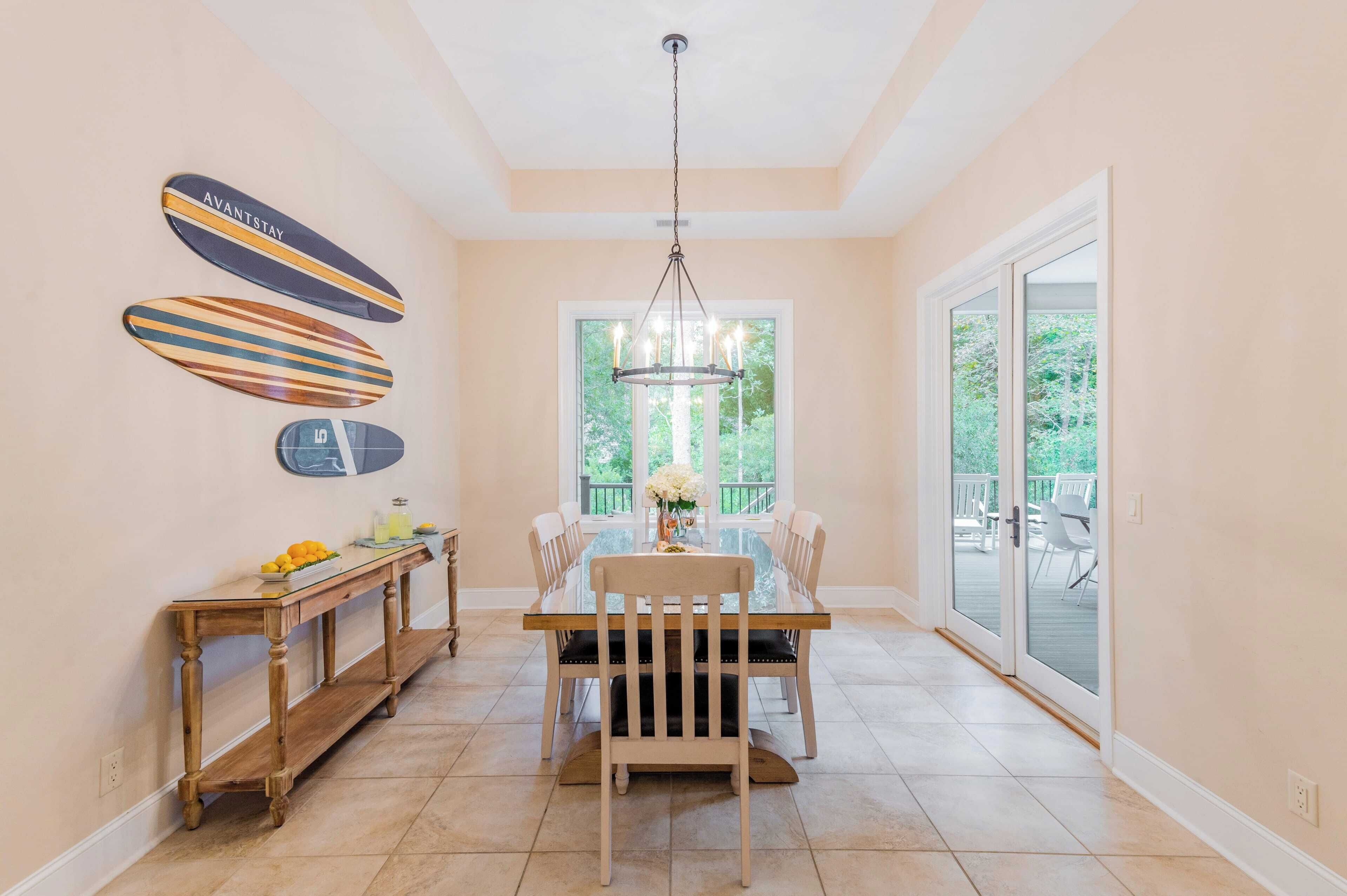 A dining area with a glass table, wooden chairs, a wooden console table with fruit, and surfboards on the wall.