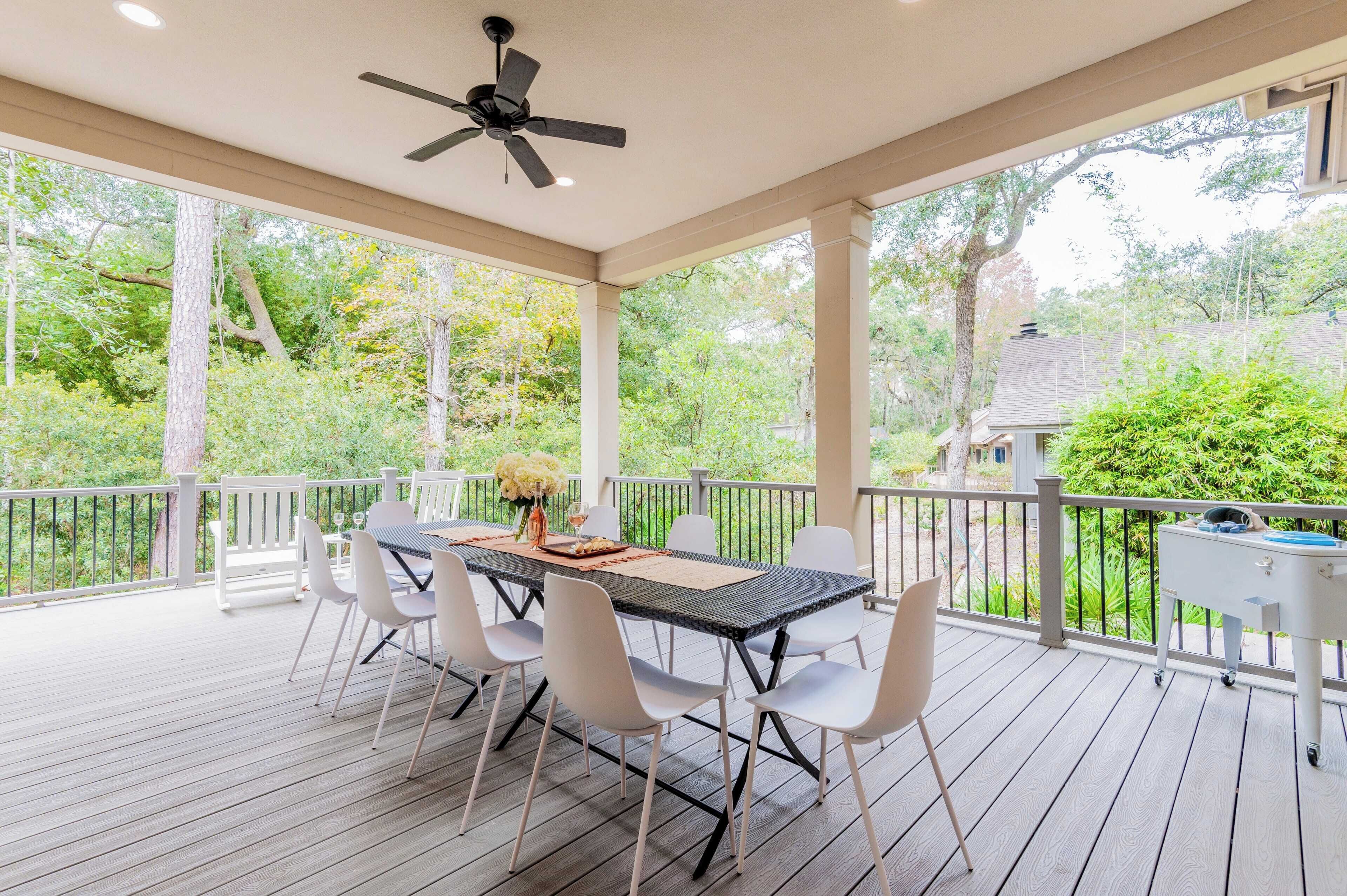 Une terrasse extérieure couverte, dotée d’une table et de chaises, d’un ventilateur de plafond et offrant une vue sur un jardin.