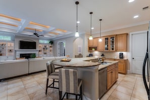 A modern kitchen with a central island, bar stools, wooden cabinets, and pendant lighting.