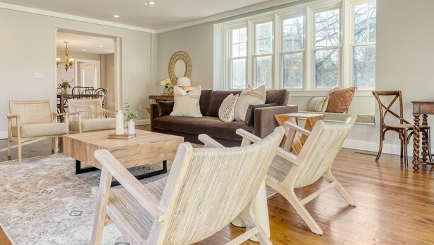 Un salon spacieux avec un canapé marron, des fauteuils en osier, une table basse en bois et une grande fenêtre à carreaux.