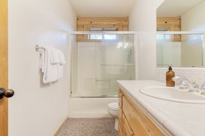 Une salle de bain avec une douche à parois de verre, un lavabo blanc et des meubles en bois.