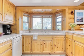 A kitchen with wooden cabinets, a dishwasher, a sink, and a window with a view of trees.
